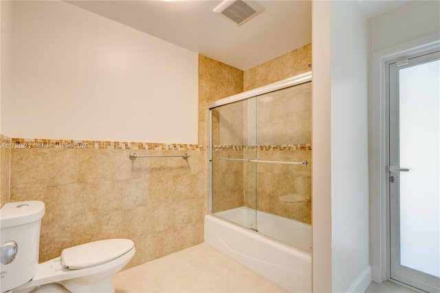 bathroom featuring tile patterned flooring, toilet, bath / shower combo with glass door, and tile walls