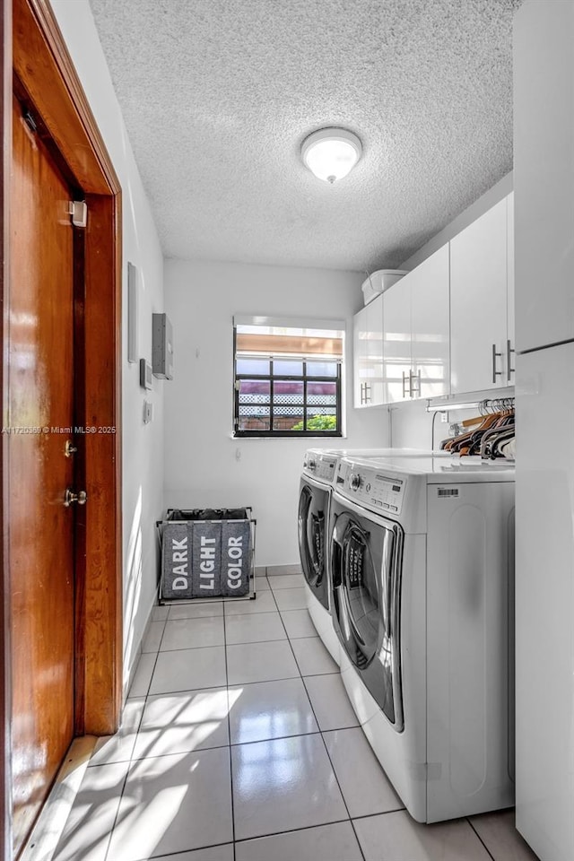 clothes washing area featuring cabinets, light tile patterned floors, a textured ceiling, and washing machine and dryer