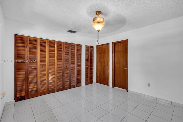 unfurnished bedroom featuring light tile patterned floors, a textured ceiling, two closets, and ceiling fan