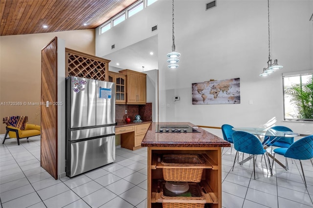 kitchen featuring a high ceiling, backsplash, stainless steel fridge, pendant lighting, and black electric cooktop