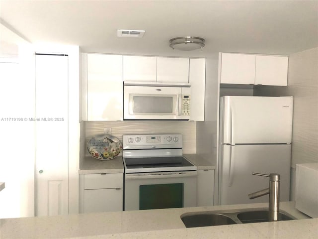 kitchen with white appliances, white cabinets, sink, tasteful backsplash, and light stone counters