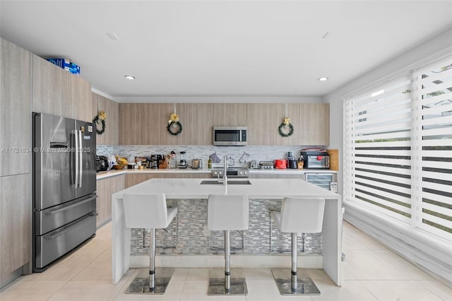 kitchen with a kitchen bar, light tile patterned floors, stainless steel appliances, and an island with sink