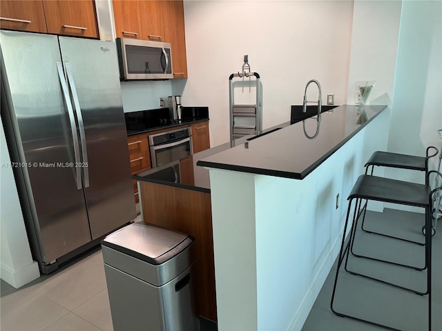 kitchen featuring a breakfast bar, light tile patterned floors, kitchen peninsula, and appliances with stainless steel finishes