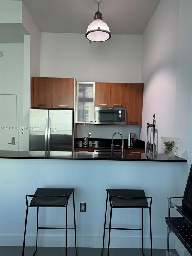 kitchen with a breakfast bar, a towering ceiling, appliances with stainless steel finishes, decorative light fixtures, and kitchen peninsula