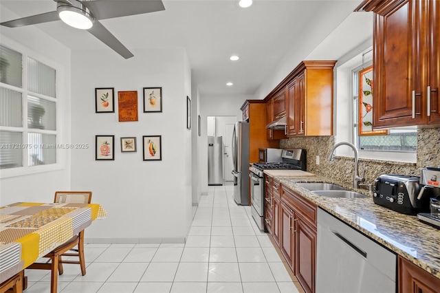 kitchen featuring light stone countertops, backsplash, stainless steel appliances, sink, and range hood