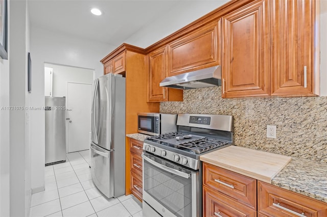 kitchen with light stone countertops, appliances with stainless steel finishes, tasteful backsplash, ventilation hood, and light tile patterned floors