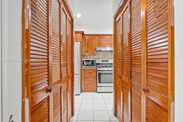 kitchen with backsplash, light tile patterned flooring, range hood, and appliances with stainless steel finishes