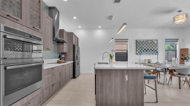 kitchen with a center island with sink, wall chimney range hood, sink, a kitchen bar, and stainless steel appliances