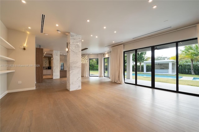 unfurnished living room featuring decorative columns and light wood-type flooring