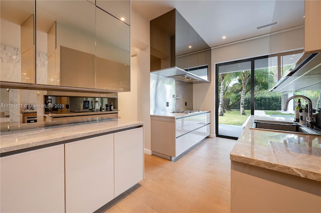 kitchen featuring wall chimney exhaust hood, sink, stainless steel gas stovetop, light stone countertops, and backsplash