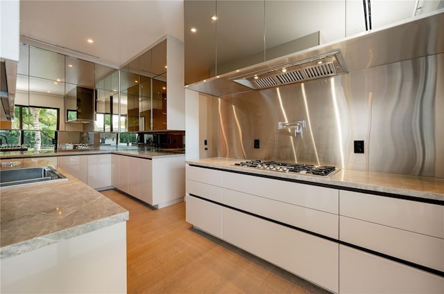 kitchen with cooktop, white cabinetry, stainless steel gas stovetop, light stone countertops, and backsplash