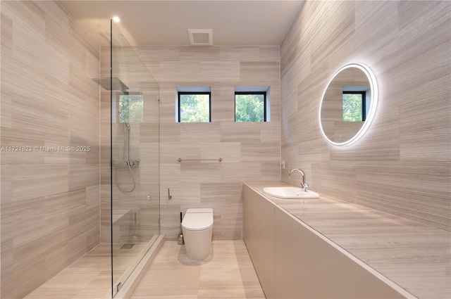 bathroom with sink, a tile shower, tile walls, and toilet