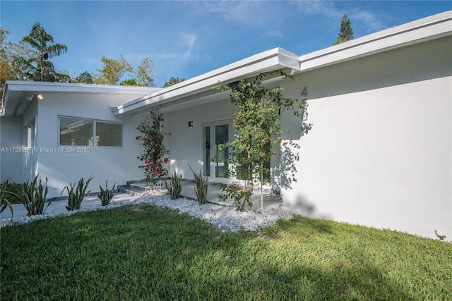 property entrance with a patio, french doors, a lawn, and stucco siding