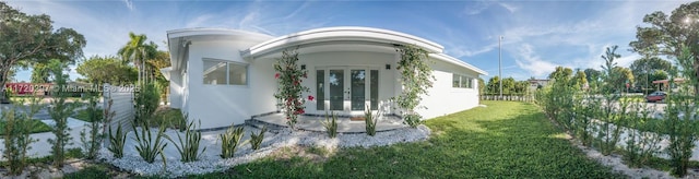 view of property exterior with french doors, a yard, and stucco siding