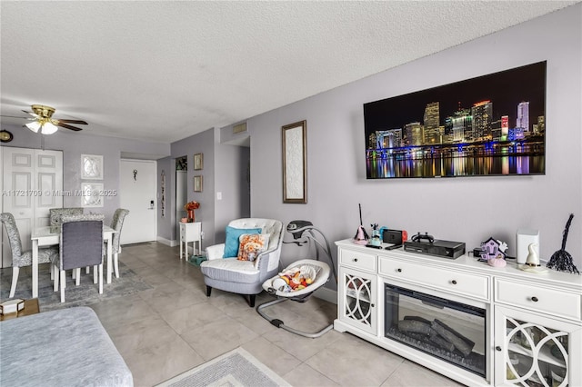 living room featuring ceiling fan, light tile patterned floors, and a textured ceiling