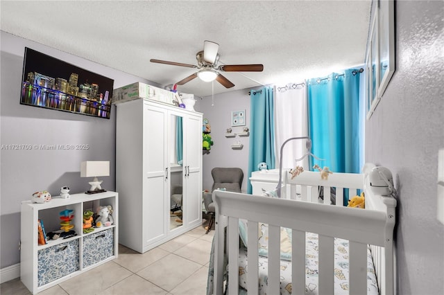 bedroom with ceiling fan, a crib, a textured ceiling, and light tile patterned floors