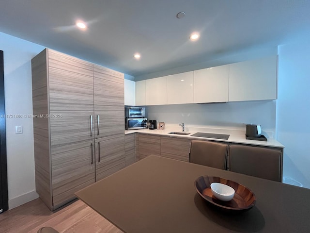 kitchen with black electric stovetop, light hardwood / wood-style flooring, white cabinets, and sink