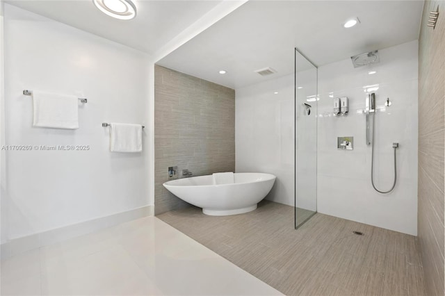 full bathroom featuring a walk in shower, a freestanding bath, visible vents, and tile walls