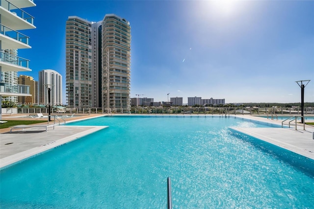 community pool with a patio, a water view, a view of the beach, and a city view