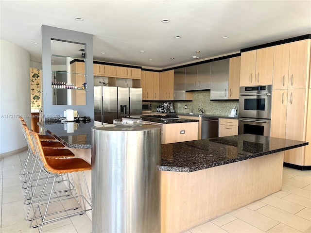 kitchen with dark stone counters, a breakfast bar area, light brown cabinetry, tasteful backsplash, and stainless steel appliances