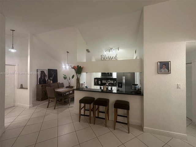 kitchen with kitchen peninsula, a towering ceiling, stainless steel appliances, light tile patterned floors, and decorative light fixtures