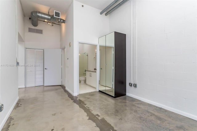 interior space featuring concrete flooring, a high ceiling, and toilet