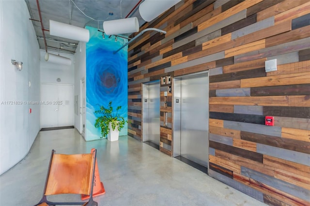 hallway with elevator, wood walls, concrete flooring, and a high ceiling