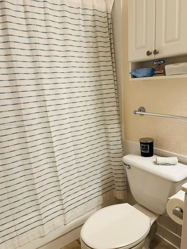 bathroom with a shower with curtain, a textured wall, and toilet