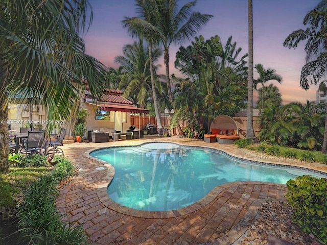 pool at dusk with a patio and exterior fireplace