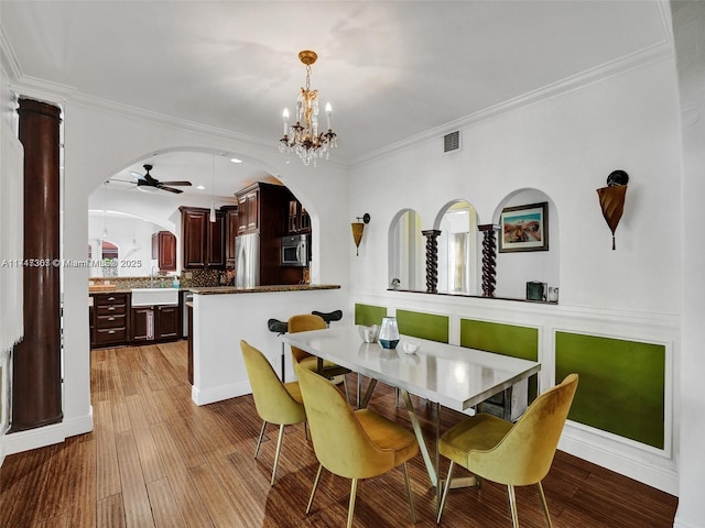 dining area with light wood-type flooring, ceiling fan with notable chandelier, crown molding, and sink