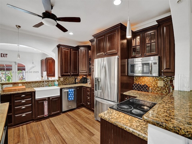 kitchen with appliances with stainless steel finishes, light wood-type flooring, backsplash, sink, and hanging light fixtures