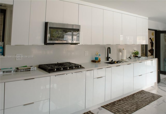 kitchen with white cabinets, gas cooktop, tasteful backsplash, and sink