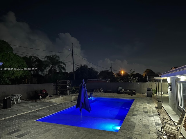 pool at night featuring a patio area