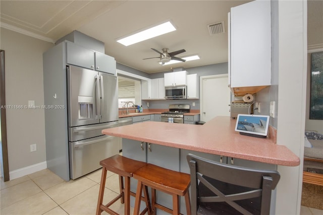 kitchen featuring ceiling fan, ornamental molding, light tile patterned flooring, white cabinetry, and stainless steel appliances