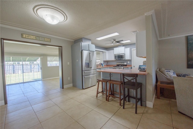 kitchen featuring a breakfast bar, appliances with stainless steel finishes, white cabinetry, light tile patterned flooring, and kitchen peninsula