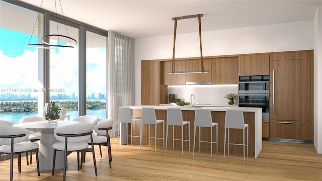 kitchen with floor to ceiling windows, hanging light fixtures, light hardwood / wood-style flooring, a breakfast bar, and a water view