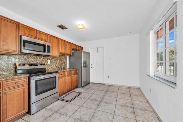 kitchen featuring stainless steel appliances, dark stone countertops, decorative backsplash, and light tile patterned floors