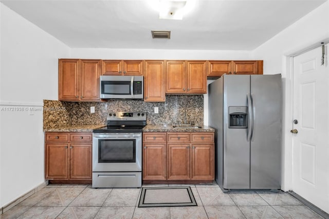 kitchen featuring sink, stone counters, light tile patterned floors, backsplash, and appliances with stainless steel finishes