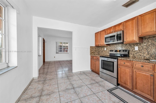 kitchen featuring appliances with stainless steel finishes, dark stone countertops, and backsplash