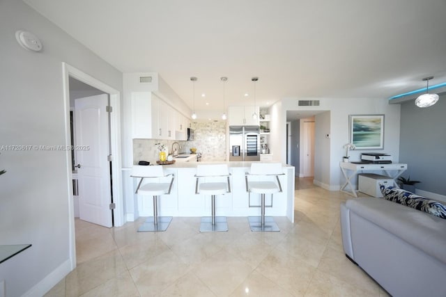 kitchen with stainless steel fridge, white cabinets, light countertops, a kitchen bar, and pendant lighting