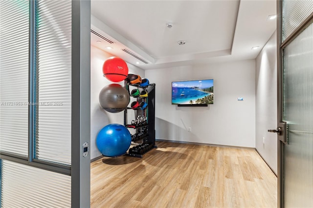 workout area with a tray ceiling and light hardwood / wood-style floors