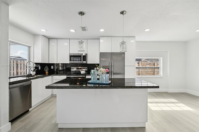 kitchen with white cabinets, appliances with stainless steel finishes, a center island, and decorative light fixtures