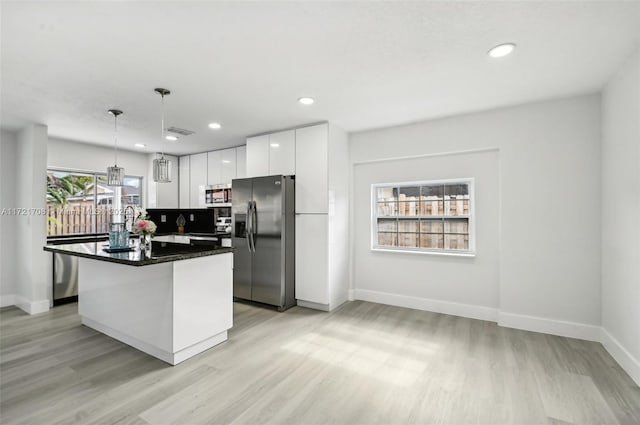 kitchen featuring decorative backsplash, stainless steel appliances, white cabinets, a center island, and hanging light fixtures