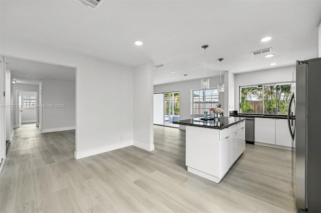 kitchen with appliances with stainless steel finishes, light hardwood / wood-style flooring, white cabinets, a center island, and hanging light fixtures