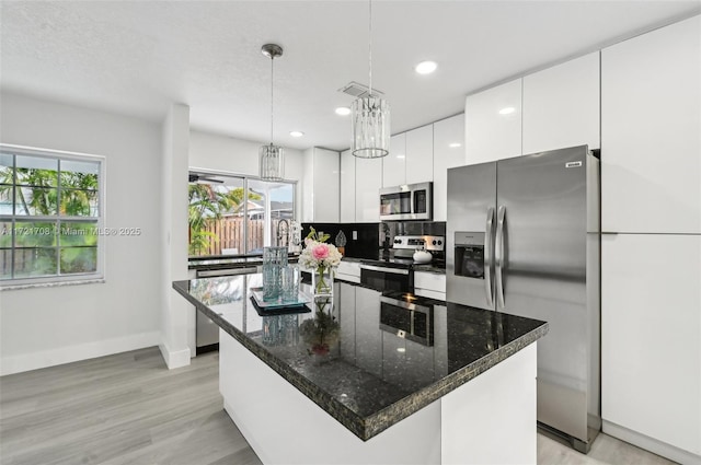 kitchen with white cabinetry, a kitchen island, decorative light fixtures, and appliances with stainless steel finishes