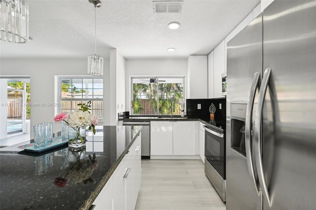 kitchen with decorative backsplash, appliances with stainless steel finishes, dark stone countertops, white cabinets, and hanging light fixtures