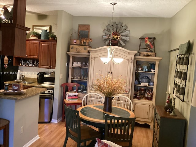 dining area with a textured ceiling, light hardwood / wood-style floors, an inviting chandelier, and sink