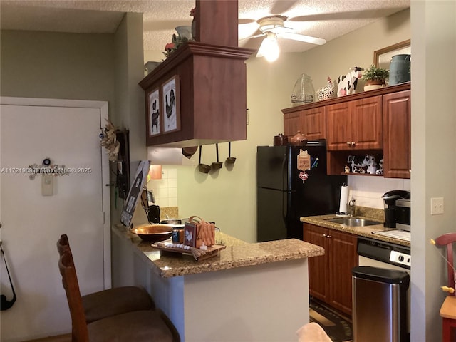 kitchen featuring black refrigerator, backsplash, light stone counters, a textured ceiling, and sink