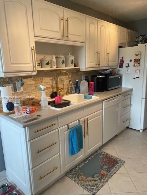 kitchen with decorative backsplash, white appliances, sink, light tile patterned floors, and white cabinets