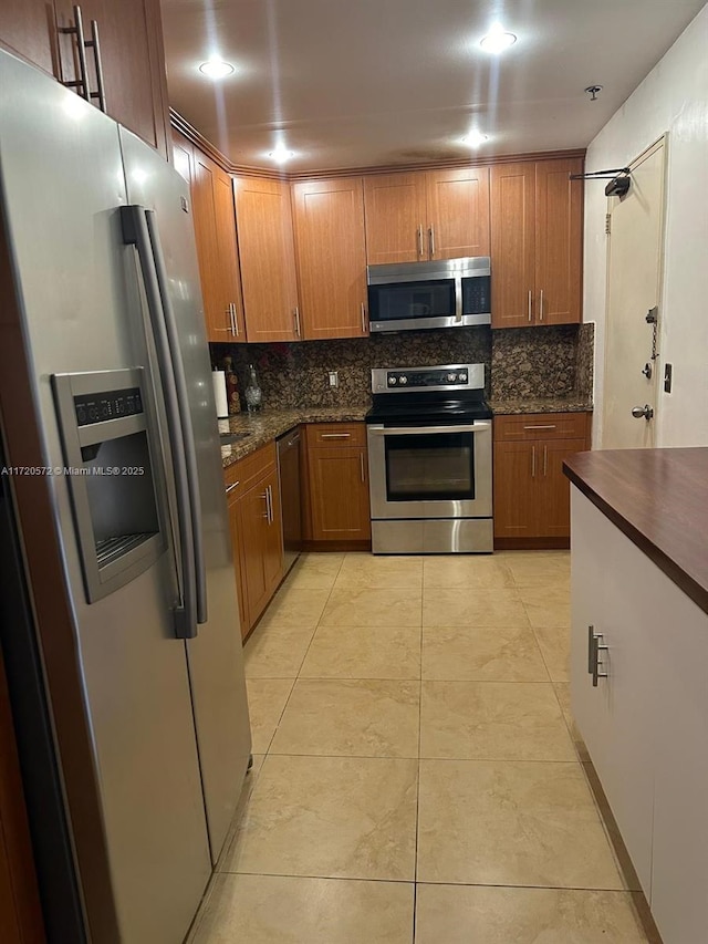 kitchen with light tile patterned floors, backsplash, stainless steel appliances, and dark stone countertops